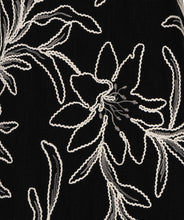 Load image into Gallery viewer, Close-up of black fabric with white floral embroidery.
