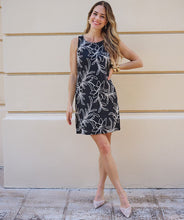 Load image into Gallery viewer, Woman wearing a black sleeveless dress with off-white floral pattern and natural heels against a beige wall.
