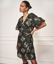 Load image into Gallery viewer, Woman wearing a black and silver puff sleeve jacquard dress against a white wall.
