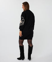 Load image into Gallery viewer, Woman wearing a black dress with floral designs and black knee-high boots against a white background.
