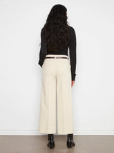 Load image into Gallery viewer, A woman shown from the back wearing high-waisted, wide-leg beige trousers with a thin dark belt, a black long-sleeve top, and black ankle boots, standing against a white wall.
