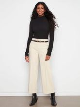 Load image into Gallery viewer, A woman modeling a black long-sleeve mock neck top and beige wide-leg cropped pants with a thin brown belt, paired with black ankle boots, against a white wall.
