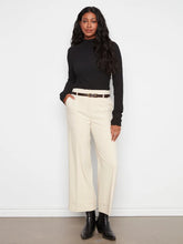 Load image into Gallery viewer, A woman modeling a black ribbed long-sleeve mock neck top and cream wide-leg cropped trousers with a thin brown belt, paired with black ankle boots, against a white wall.
