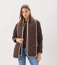Load image into Gallery viewer, A woman modeling a dark brown diamond-quilted jacket with cream-colored trim along the edges  styled with a brown ribbed top and blue jeans against a plain light gray background.
