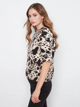Load image into Gallery viewer, Woman wearing a black, brown and off-white cow print top and black jeans against a plain background.
