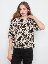 Load image into Gallery viewer, Woman wearing a black, brown and off-white cow print top and black jeans against a plain background.
