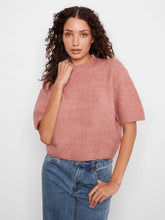 Load image into Gallery viewer, A woman with curly brown hair wearing a dusty rose short-sleeve knit top and blue jeans, standing against a light gray studio background.
