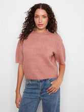 Load image into Gallery viewer, A woman with curly brown hair wearing a dusty rose short-sleeve knit top and blue jeans, standing against a light gray studio background.
