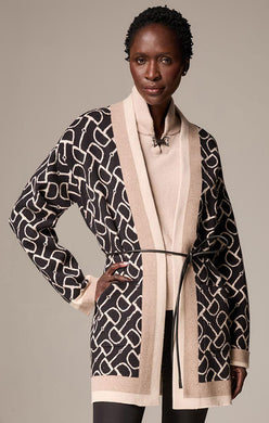 Woman wearing a neutral and black long jacket over a riding sweater and black tights against a neutral background.