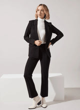Load image into Gallery viewer, Woman wearing a black suit with white top and white boots against a white background.
