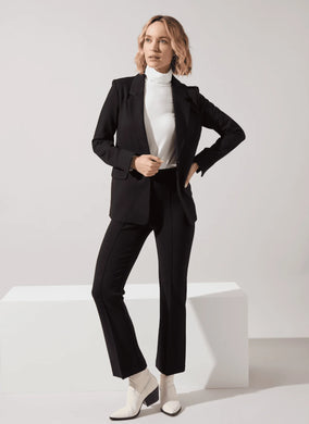 Woman wearing a black suit with white top and white boots against a white background.