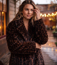 Load image into Gallery viewer, A woman wearing a plush brown leopard-print faux fur coat, standing outdoors on a wet street with warm bokeh lights in the background.
