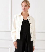 Load image into Gallery viewer, Woman wearing an off-white jacket over a black jumpsuit standing in front of a white wall.
