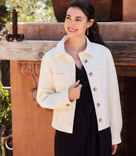 Load image into Gallery viewer, Woman wearing an off-white jacket over a black jumpsuit standing outdoors against a fireplace.
