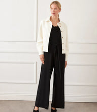 Load image into Gallery viewer, Woman wearing an off-white jacket over a black jumpsuit standing in front of a white wall.
