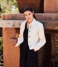 Load image into Gallery viewer, Woman wearing an off-white jacket over a black jumpsuit standing outdoors against a fireplace.
