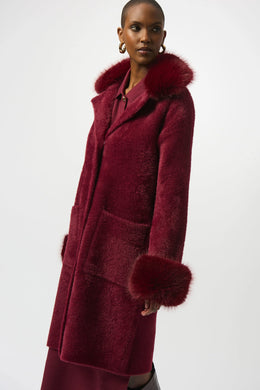 Woman wearing a burgundy coat with fur trim against a white background.