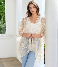 Load image into Gallery viewer, Woman wearing a floral gold and off-white kimono over a white top and blue jeans, standing against a column.
