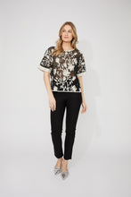 Load image into Gallery viewer, Woman wearing a sheer black embroidered floral patterned sequin short sleeve top, black pants and silver heels against a white background.
