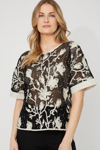 Load image into Gallery viewer, Woman wearing a sheer black embroidered floral patterned sequin short sleeve top and black pants against a white background.
