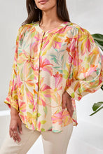 Load image into Gallery viewer, Woman wearing a colorful blouse, white pants standing in a bright room with a plant.
