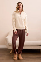 Load image into Gallery viewer, Woman wearing a moonstone zip up sweater, brown pants and brown shoes standing in a room with a beige couch.
