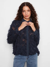 Load image into Gallery viewer, Woman modeling a navy blouse with fringe detailing and blue jeans against a white wall.
