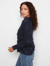 Load image into Gallery viewer, A woman standing sideways modeling a navy blouse with fringe detailing and blue jeans against a white wall.
