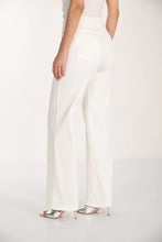 Load image into Gallery viewer, Woman wearing a white floral top off -white jeans and silver sandals against a white background.
