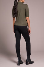 Load image into Gallery viewer, Woman wearing a spruce green short sleeve top, black pants and black boots against a neutral background.
