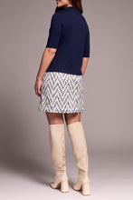 Load image into Gallery viewer, Woman wearing a navy top, patterned skirt, and beige knee-high boots against a neutral background.
