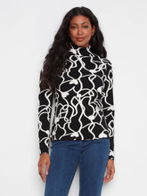 Load image into Gallery viewer, A woman modeling a black and white abstract wavy pattern mock neck sweater with blue jeans, set against a plain light gray background.
