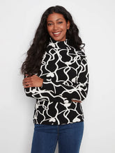 Load image into Gallery viewer, A woman with long, wavy black hair is wearing a black mock-neck long-sleeve top with a white abstract wavy line pattern, paired with blue jeans, against a plain white studio background.
