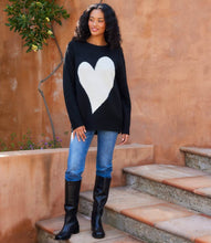 Load image into Gallery viewer, Woman wearing a black sweater with a white heart design, blue jeans, and black boots standing on steps.
