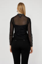 Load image into Gallery viewer, Woman wearing a black sheer top with geometric pattern and black pants against a white background.

