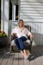 Load image into Gallery viewer, Woman sitting on a wicker chair on a wooden deck with a white house in the background.
