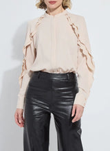 Load image into Gallery viewer, Model wearing a rose petal colored blouse with ruffle detailing and black pants against a white background.
