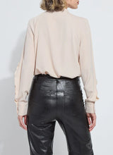 Load image into Gallery viewer, Model wearing a rose petal colored blouse with ruffle detailing and black pants against a white background.
