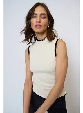 Woman wearing an ivory sleeveless top with black trim and black pants against a light gray background.