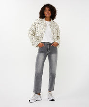 Load image into Gallery viewer, Woman wearing an off-white and silver sequin bomber jacket over a white top, grey jeans and white sneakers against a white background.
