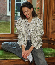 Load image into Gallery viewer, Woman sitting on a bench in front of a window wearing an off-white and silver sequin bomber jacket, grey jeans and white sneakers.
