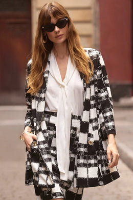 Woman walking on a street wearing a black and white plaid blazer, matching skirt, white shirt and sunglasses.