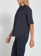 Load image into Gallery viewer, A woman wearing a dark navy blue short-sleeve button-up shirt with rolled cuffs and dark blue jeans, shown from a side profile against a plain light gray background.
