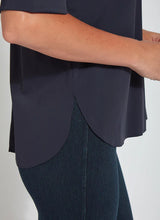 Load image into Gallery viewer, Close-up of a person wearing a dark navy short-sleeve top with a curved hem and dark teal leggings against a plain light background.
