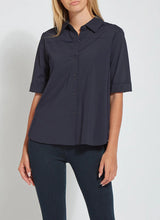 Load image into Gallery viewer, A woman wearing a dark navy blue short-sleeve button-up shirt with rolled cuffs and dark blue jeans, shown from the chin down against a light gray studio background.
