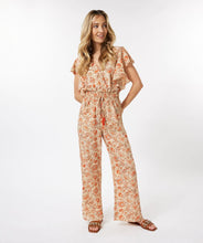 Load image into Gallery viewer, A breathtaking blend of orange, brown and red floral motifs on a pastel peach backdrop define the fashionable aura of the Tinslee jumpsuit. Delicate gold accents adorn the piece, accentuating the visual appeal of the design. For added drama, it features ruffled sleeves and an elasticized waist with tassels to give it a captivating, effortless style.  Color- Orange, brown, red, pastel peach, gold. One piece. Elasticized waist with tassels. V-neck. Ruffle sleeves. Fabric- 100% Polyester.
