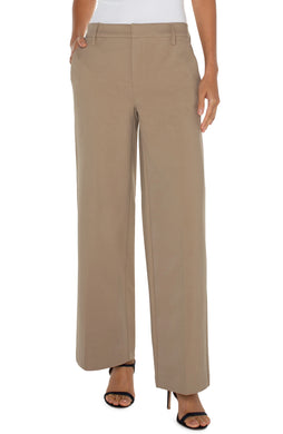 Model wearing beige trousers, white top and black heels against a white background.