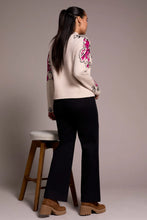 Load image into Gallery viewer, Woman wearing a pink and black floral sweater, black pants and brown boots standing next to a wooden stool against a plain background.
