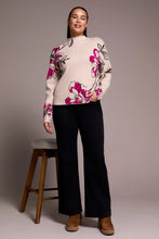 Load image into Gallery viewer, Woman wearing a pink and black floral sweater, black pants and brown boots standing next to a wooden stool against a plain background.
