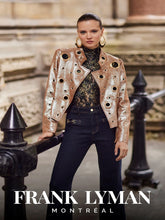 Load image into Gallery viewer, Model wearing a navy and gold floral lace top with a gold jacket and denim pants standing against a black iron barrier in front of a stone building.
